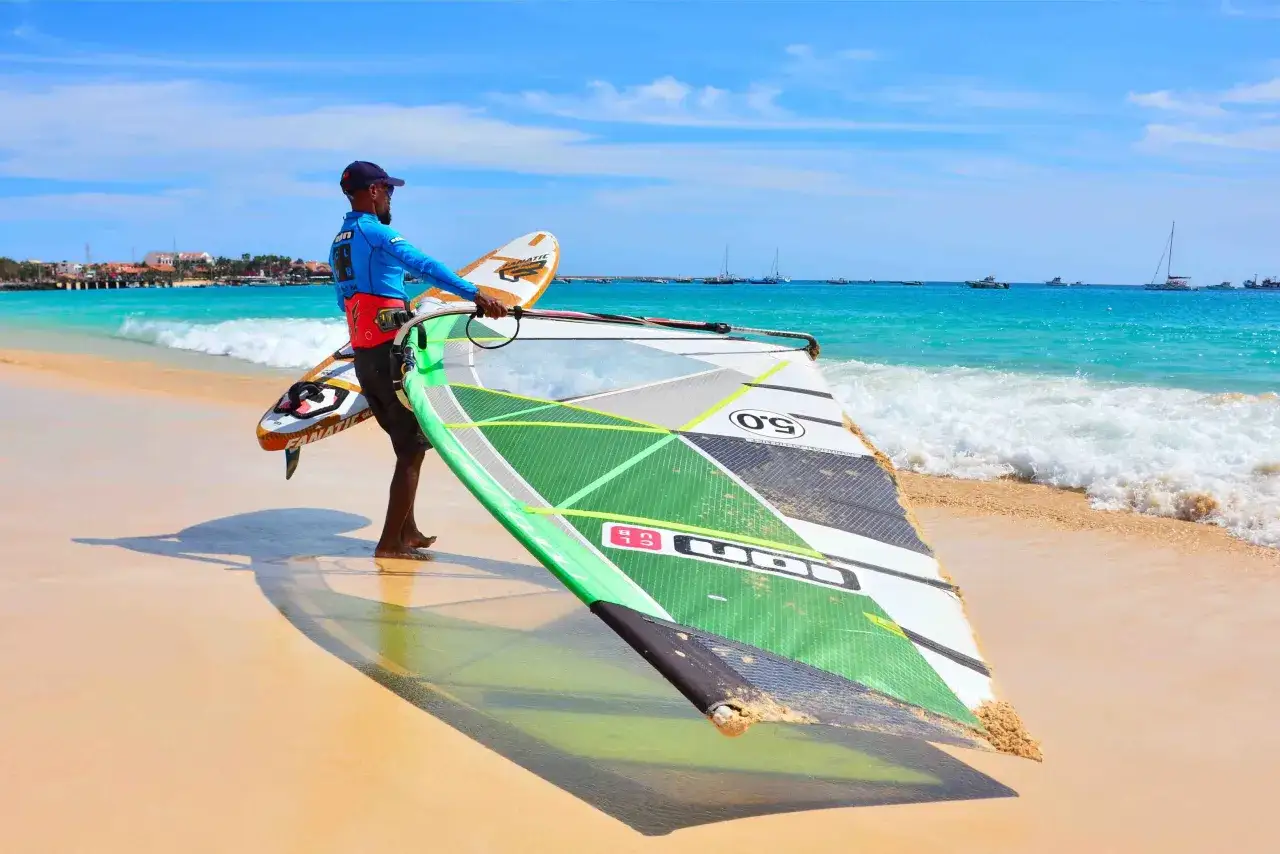 Mann mit Windsurf-Ausr&uuml;stung am Strand der Kapverden, bereit f&uuml;r das Windsurfen Kapverden.