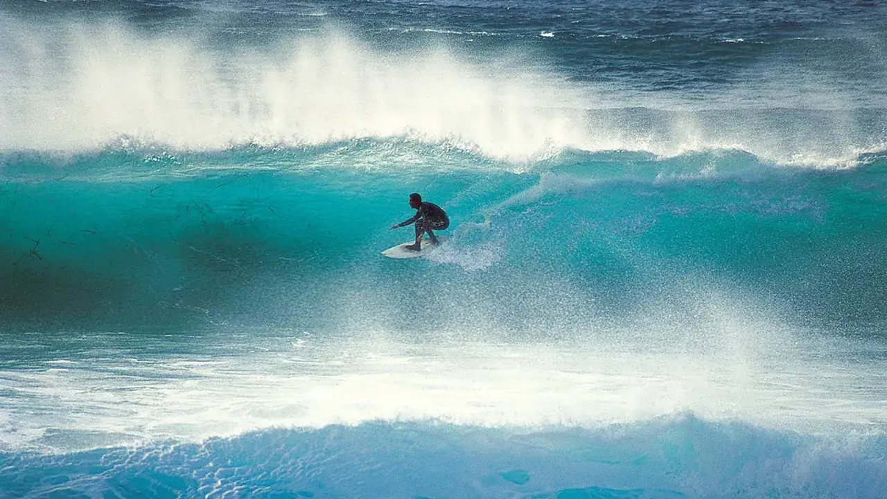 Ein Surfer reitet eine türkise Welle, die Gischt spritzt. Ein perfekter Tag für Capo Mannu Surf.