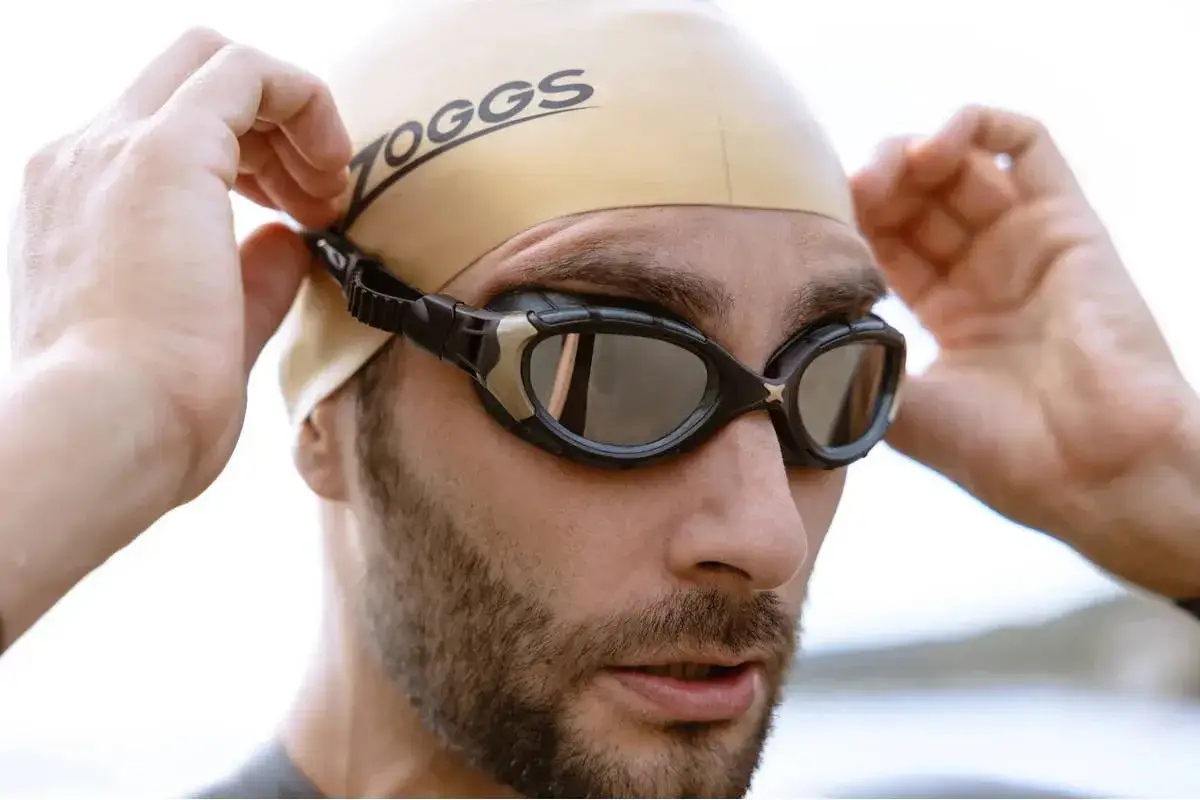 Mann mit Badedut und Schwimmbrille, die er sich zurechtrückt. Perfekt für die Schwimmbrille reinigen.