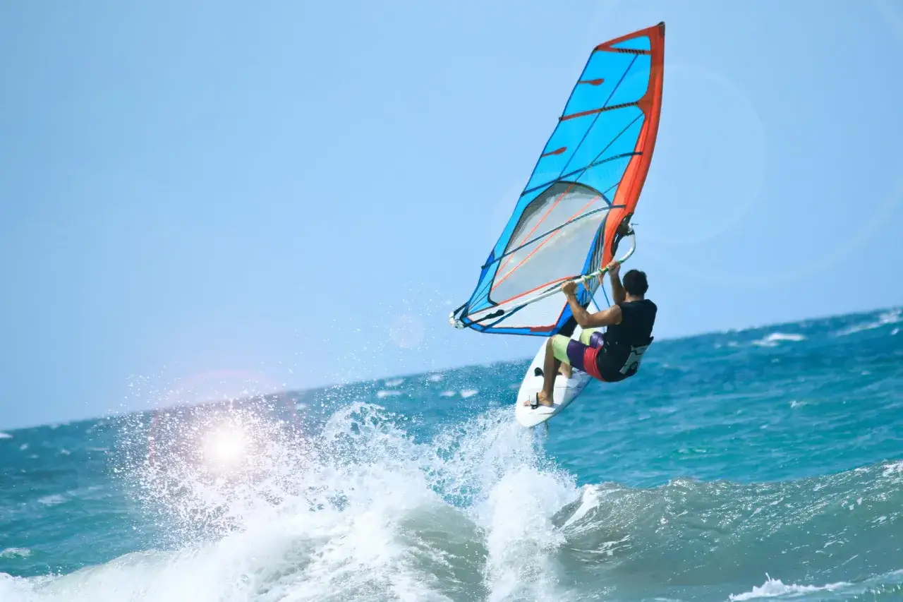 Ein Windsurfer springt &uuml;ber eine Welle im t&uuml;rkisfarbenen Meer. Das bunte Segel leuchtet in der Sonne. Ein perfekter Tag zum Windsurfen Kroatien!