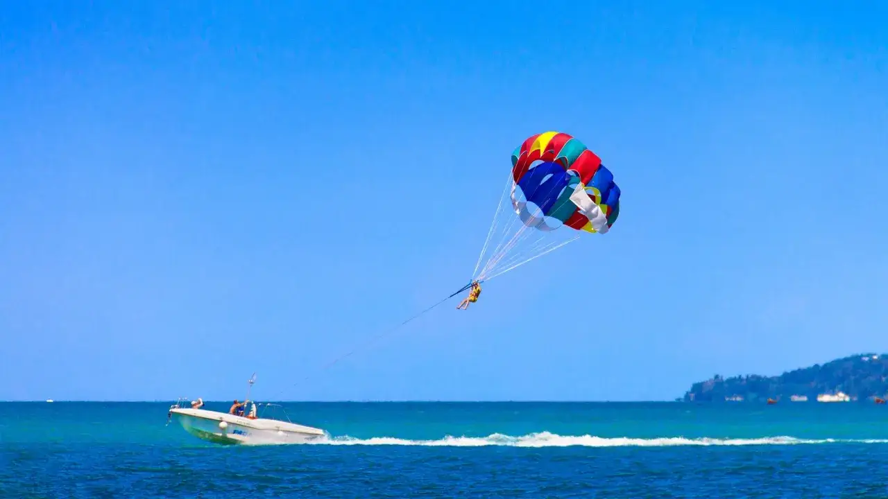 Buntes Parasegel zieht Person über blaues Meer, während Boot fährt. Tolle Wassersport Europa Erfahrungen!