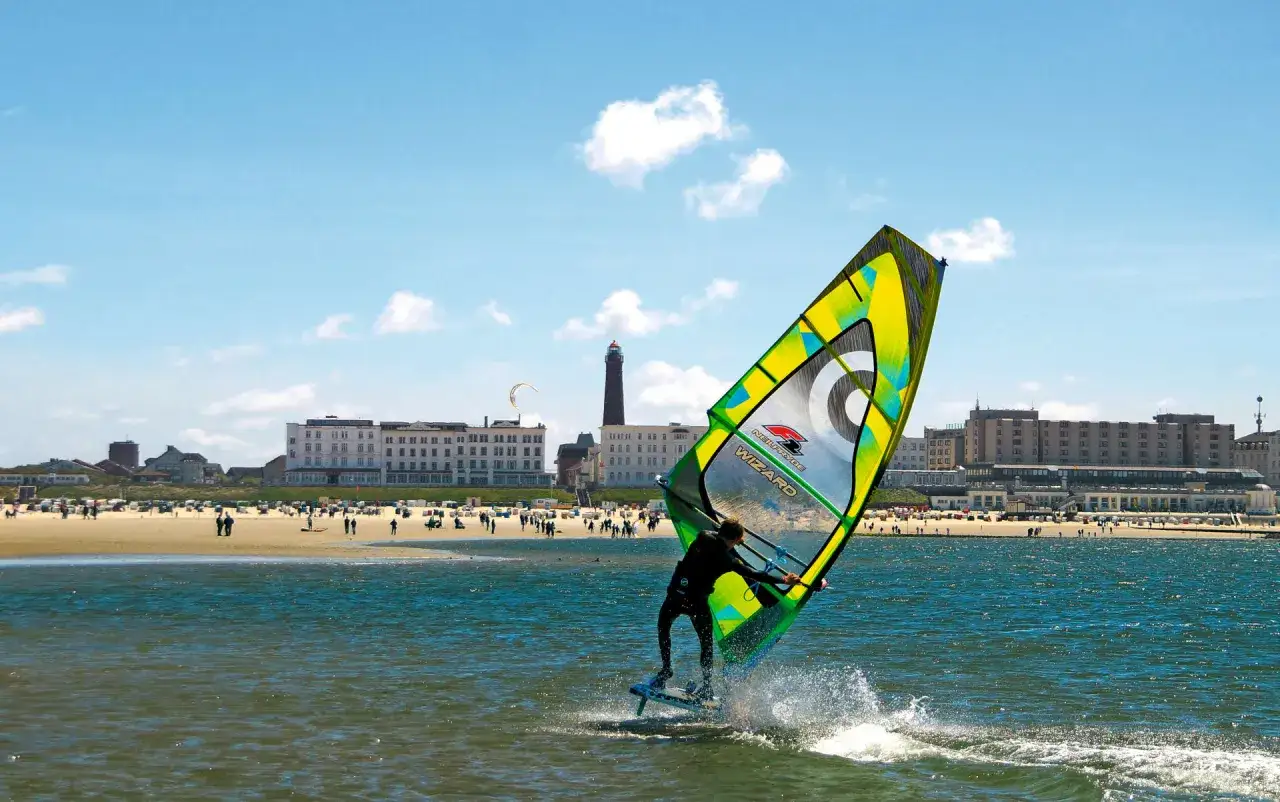 Windsurfer auf dem Wasser vor Borkum, im Hintergrund der Strand mit Menschen und Gebäuden.