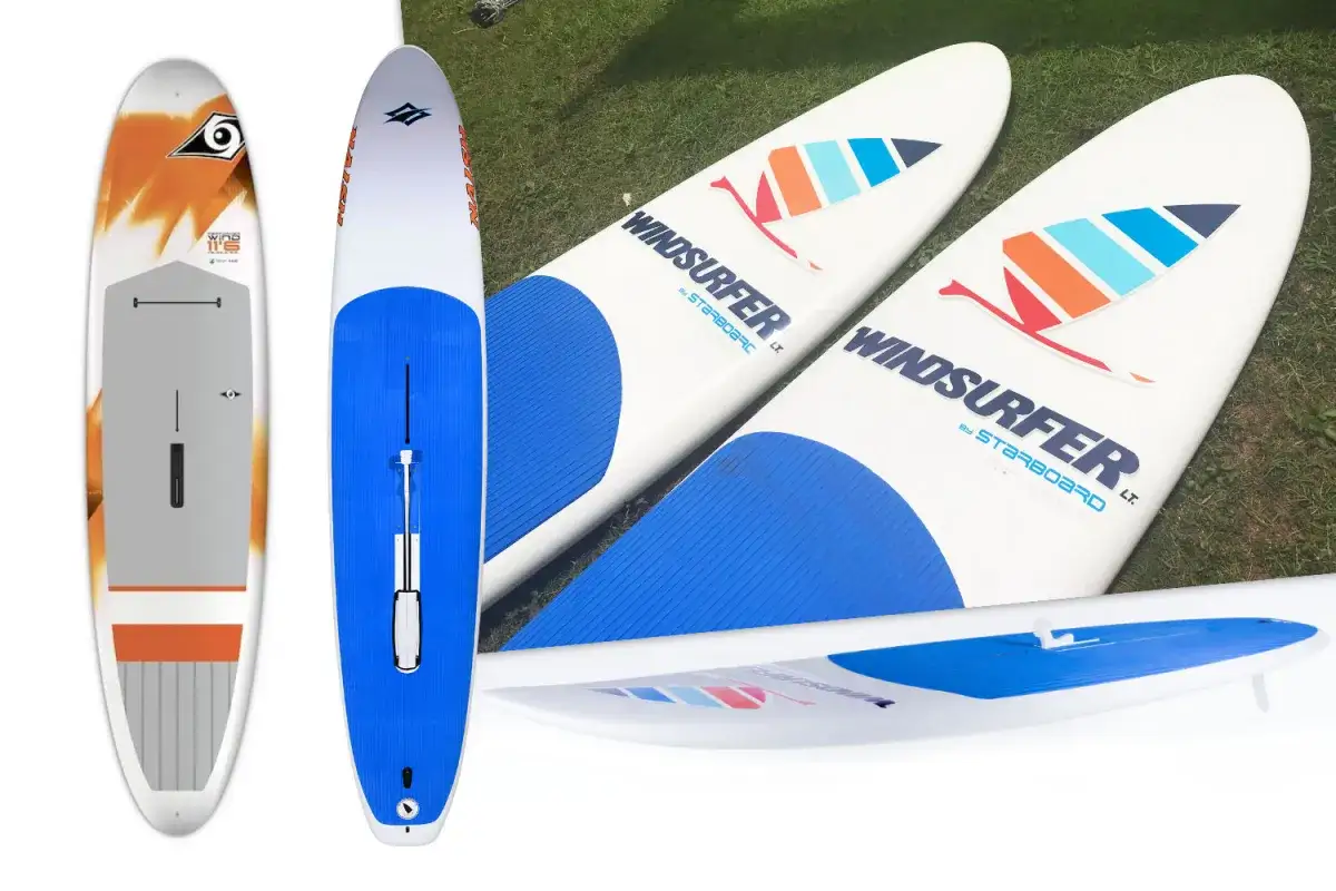 Mehrere Windsurfboards, ideal f&uuml;r Anf&auml;nger, liegen auf Gras. Eines ist wei&szlig; mit orangefarbenen Akzenten, die anderen sind wei&szlig; mit blauen und bunten Segel-Logos.