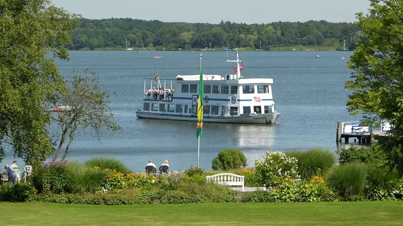 Ein Ausflugsschiff f&auml;hrt auf dem Zwischenahner Meer, umgeben von gr&uuml;nen Ufern und bl&uuml;henden Blumen.