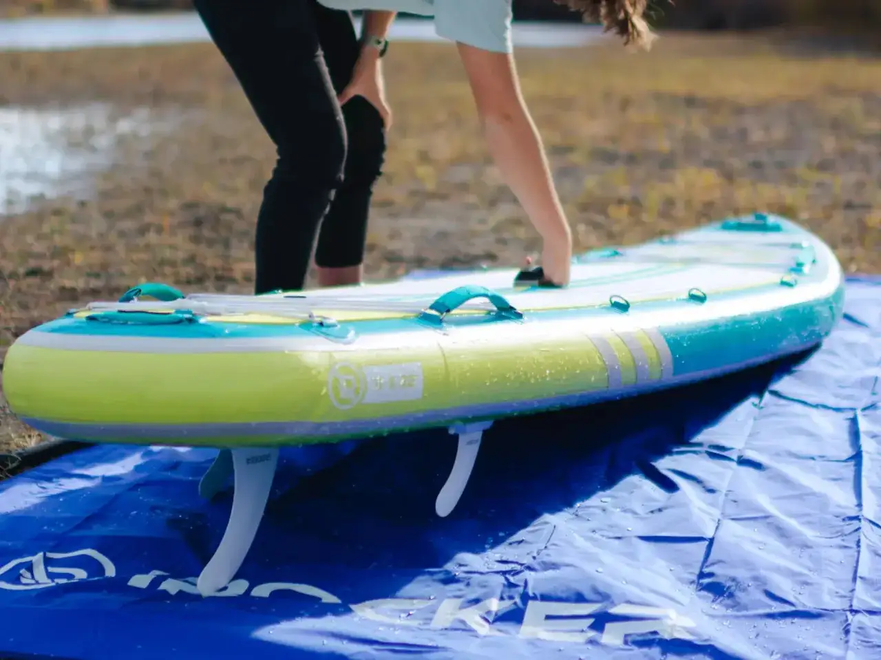 Person bereitet ein aufblasbares SUP-Board für die Pflege vor. Das Board liegt auf einer blauen Unterlage.