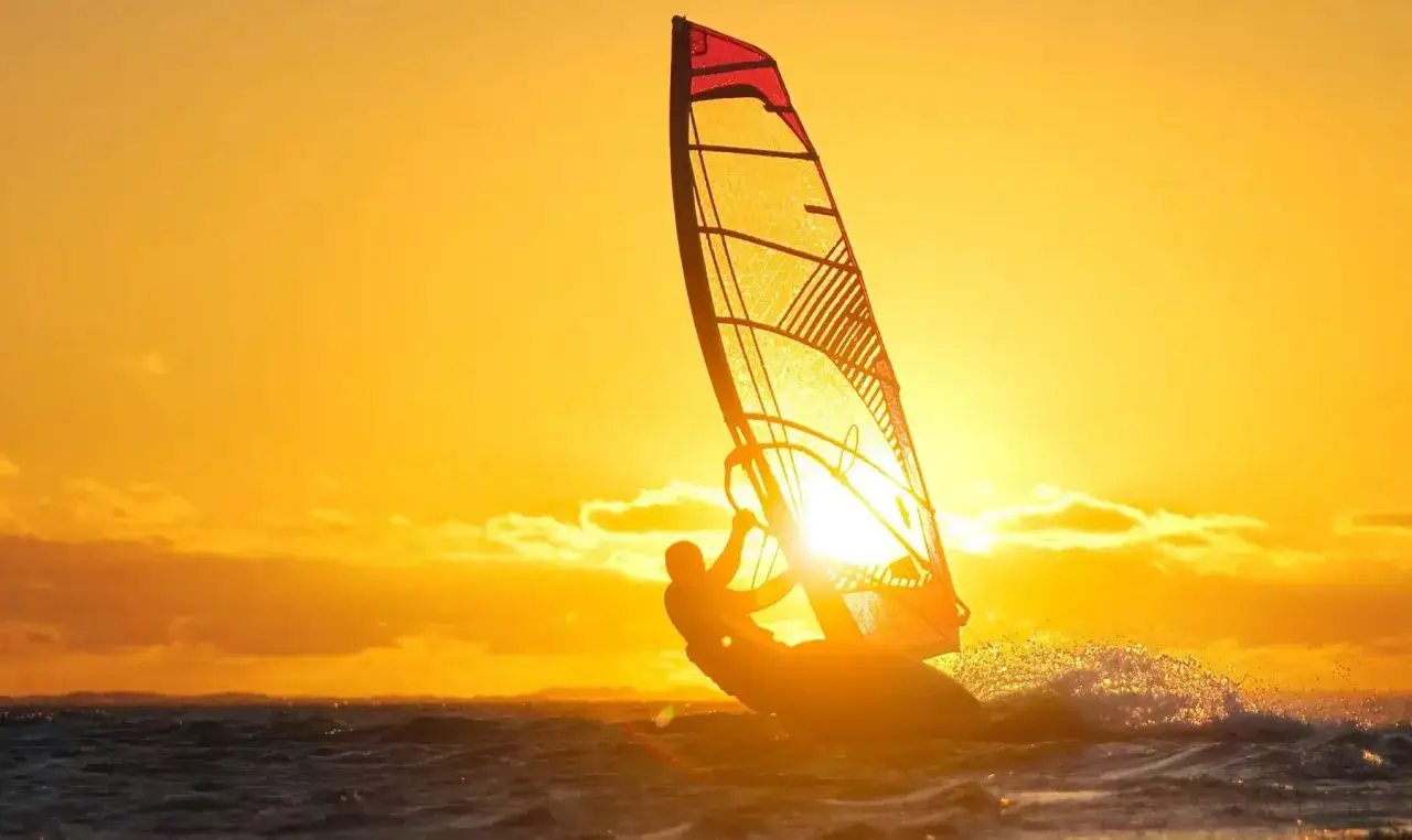 Windsurfer genie&szlig;t die untergehende Sonne am Starnberger See. Das goldene Licht taucht die Szene in warme Farben.