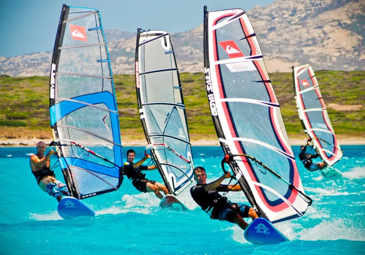 M&auml;nner beim Windsurfen in Italien, die mit ihren bunten Segeln &uuml;ber das t&uuml;rkisfarbene Meer gleiten.