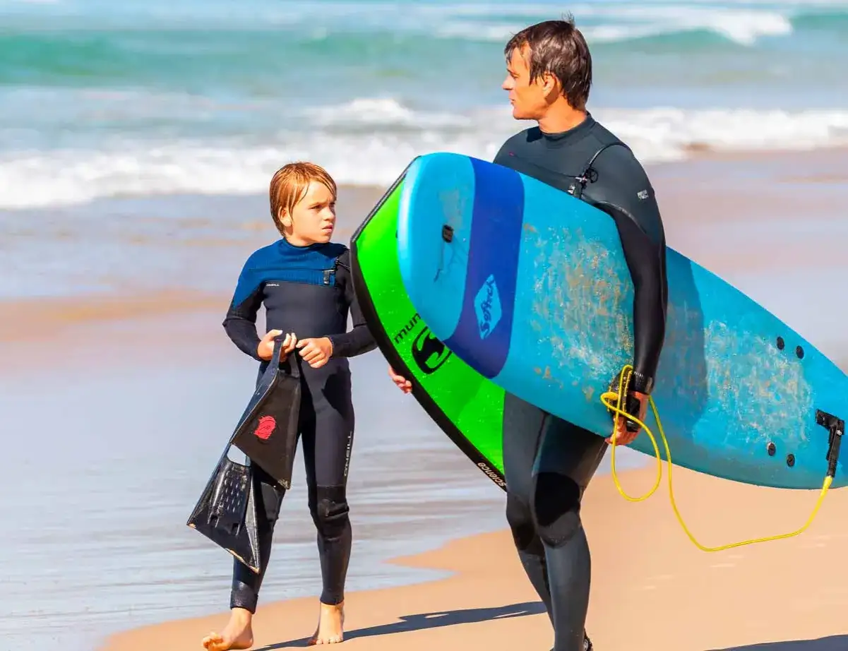 Vater und Sohn mit Surfbrett und Flossen am Strand. Ein perfekter Tag für surfbrett kinder.