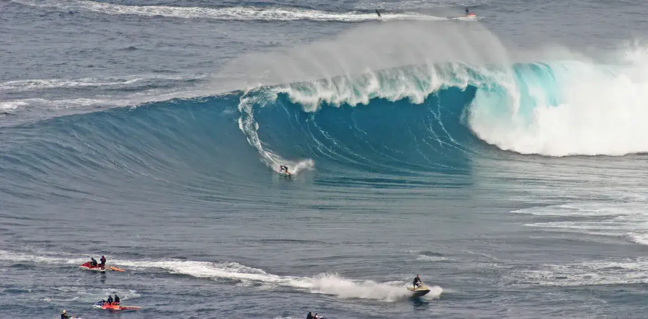 Surfer reitet eine riesige Welle bei Jaws, Hawaii. Jetskis sind in der Nähe, um bei Bedarf zu helfen.
