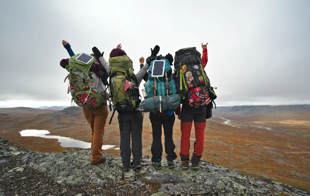 Vier Wanderer mit vollgepackten Rucks&auml;cken f&uuml;r eine Mehrtagestour stehen auf einem Felsen und blicken in eine weite Landschaft.