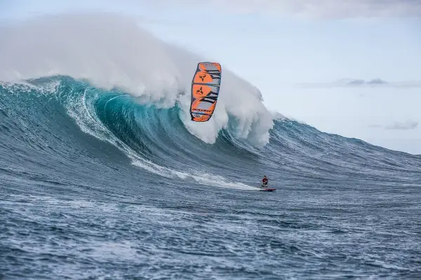 Ein Kitesurfer reitet eine riesige Welle bei Jaws, Hawaii. Die Welle bricht mit gewaltiger Kraft, während der Surfer mit seinem Kite in der Luft schwebt.
