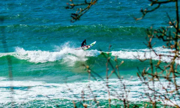 Windsurfer auf einer Welle vor Bornholm. Das türkisfarbene Meer und die Gischt erzeugen ein dynamisches Bild vom Surfen.